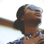 A woman wearing sunglasses, listening to her favorite songs on a Spotify playlist, and looking up at the sky.