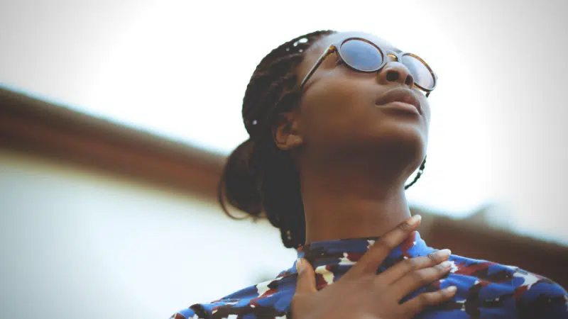 A woman wearing sunglasses, listening to her favorite songs on a Spotify playlist, and looking up at the sky.