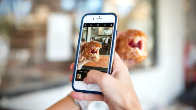 A person capturing an Instagram-worthy photo of a donut on their phone.