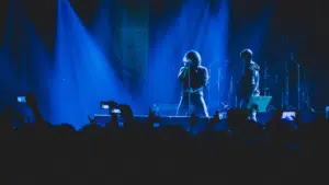 Two musicians perform on stage under blue lighting, their captivating tunes filling the air while a sea of phones rises, creating a wave of UGC as fans eagerly capture the moment.