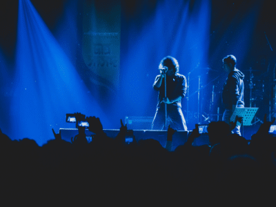 Two musicians perform on stage under blue lighting, their captivating tunes filling the air while a sea of phones rises, creating a wave of UGC as fans eagerly capture the moment.