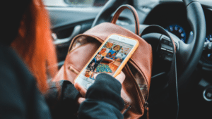 A woman in a brown backpack holding a cell phone in her car, engaged in social media.