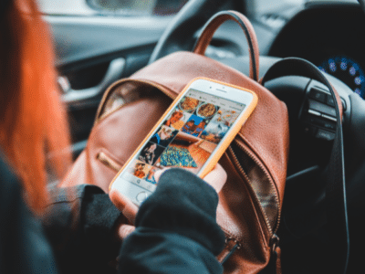 A woman in a brown backpack holding a cell phone in her car, engaged in social media.