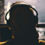 A person in a yellow hoodie with headphones, lost in the rhythm of cover songs while gazing out a window.