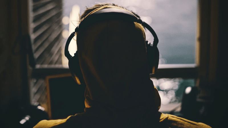 A person in a yellow hoodie with headphones, lost in the rhythm of cover songs while gazing out a window.