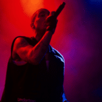 A man holding a microphone on stage in front of red and blue lights.