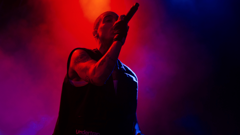 A man holding a microphone on stage in front of red and blue lights.