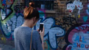 A woman scrolling through her phone in front of a wall covered in graffiti.