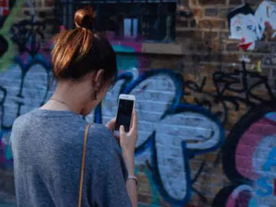 A woman scrolling through her phone in front of a wall covered in graffiti.