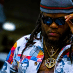 A man with dreadlocks and sunglasses is standing in a parking lot, looking like the epitome of cool, ready to invest in what matters most to musicians.