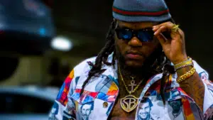 A man with dreadlocks and sunglasses is standing in a parking lot, looking like the epitome of cool, ready to invest in what matters most to musicians.