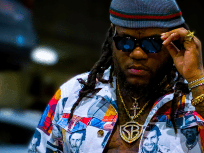 A man with dreadlocks and sunglasses is standing in a parking lot, looking like the epitome of cool, ready to invest in what matters most to musicians.