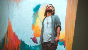 A creative man standing in front of a colorful painting.