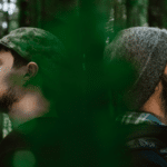 Two men in a forest looking at each other.
