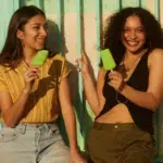 Two young women holding ice creams in front of a building.