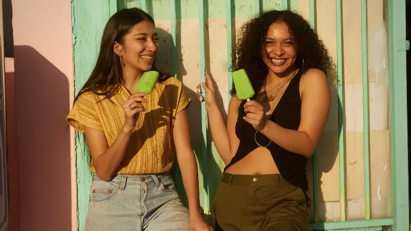 Two young women holding ice creams in front of a building.