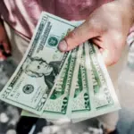 A man is holding a stack of dollar bills representing large royalties.