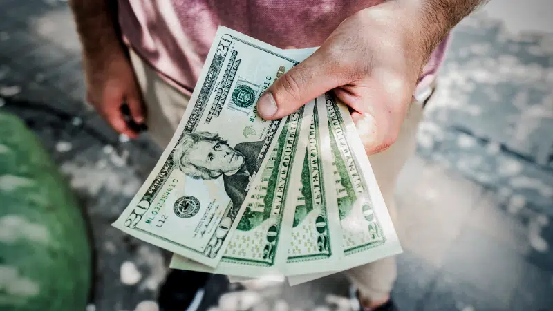 A man is holding a stack of dollar bills representing large royalties.