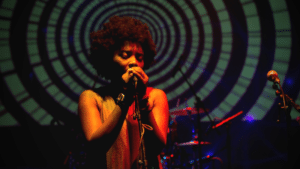 A woman singing into a microphone in front of a circular screen.