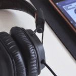 A pair of black over-ear headphones is placed next to a smartphone displaying Spotify playlists on a black mousepad.