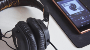 A pair of black over-ear headphones is placed next to a smartphone displaying Spotify playlists on a black mousepad.