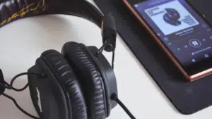 A pair of black over-ear headphones is placed next to a smartphone displaying Spotify playlists on a black mousepad.