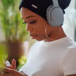 A woman wearing headphones listening to music on Spotify while glancing at her phone.