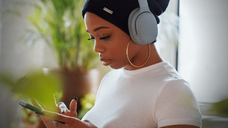 A woman wearing headphones listening to music on Spotify while glancing at her phone.