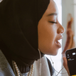 A woman wearing a hijab is listening to music on her phone.