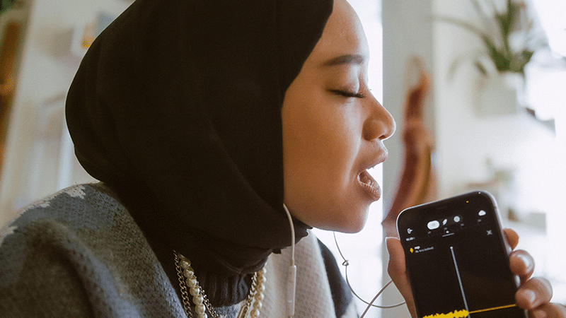 A woman wearing a hijab is listening to music on her phone.