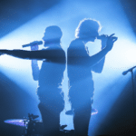Two men standing on stage in front of a blue light.