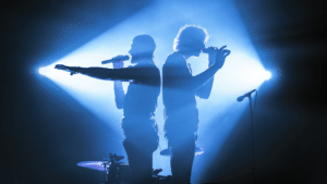 Two men standing on stage in front of a blue light.