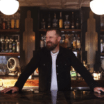 A man surrounded by liquor bottles in a bar.