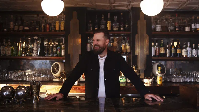 A man surrounded by liquor bottles in a bar.