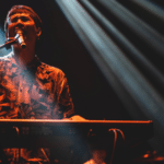 A man skillfully playing a keyboard at a concert while captivating the audience with his musical prowess.
