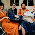A group of women sitting at an outdoor table reading a newspaper while enjoying a Jazz Spotify playlist.