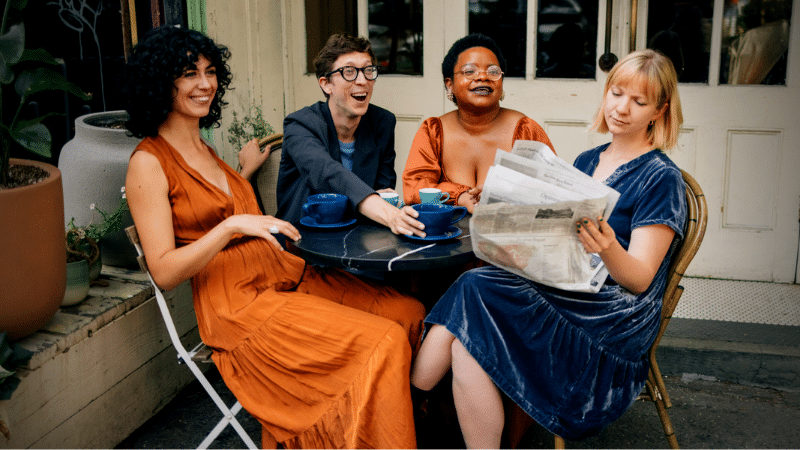 A group of women sitting at an outdoor table reading a newspaper while enjoying a Jazz Spotify playlist.