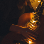 A woman playing a guitar in a dark room.