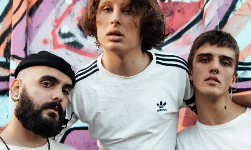 Three young men posing in front of a graffiti wall.