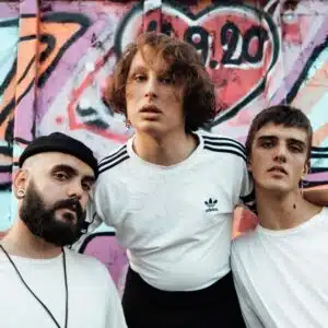 Three young men posing in front of a graffiti wall.