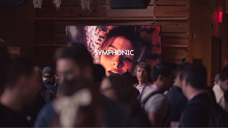A crowd of people attending a music conference standing in front of a large screen.