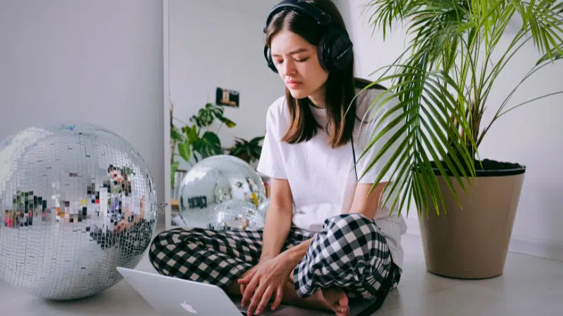 A woman wearing headphones and sitting on the floor with a laptop, utilizing productivity tools.