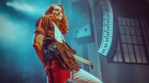 A man with long hair standing onstage playing a guitar.