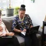 Two women sitting on a couch looking at a laptop while discussing questions to ask an attorney.