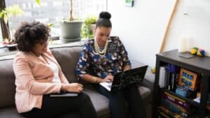 Two women sitting on a couch looking at a laptop while discussing questions to ask an attorney.