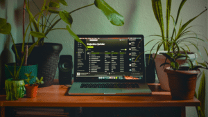 A laptop on a desk next to a potted plant while using Spotify.