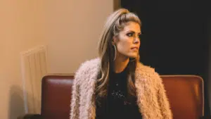 A woman in a pink fur coat listening to new music on a couch.