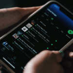 A person holding a cell phone with a social media app on it showcasing Spotify.