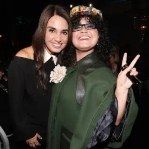 Two women smiling for the camera at a women-led music event, one making a peace sign gesture.