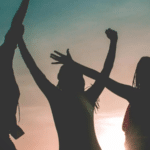 Silhouette of a group of empowered women celebrating at sunset.